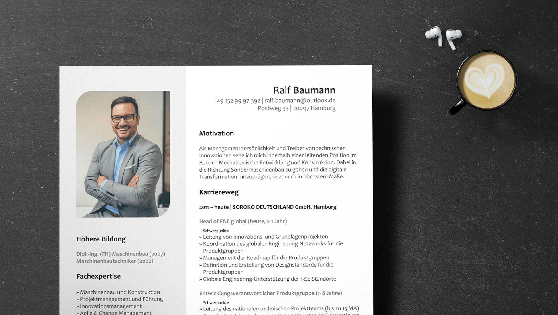 Luftaufnahme eines Lebenslaufs und eines Anschreibens auf einem dunklen Tisch mit einer Kaffeetasse mit Latte Art. Der Lebenslauf enthält ein Foto einer lächelnden Person im Anzug, Kontaktinformationen, ein Motivationsschreiben, den beruflichen Werdegang und Angaben zur Ausbildung.